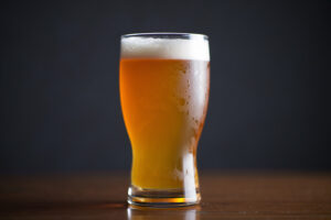 Beer Photography showing a crystal clear beer glass filled with golden amber beer sits centered on a polished dark wooden surface
