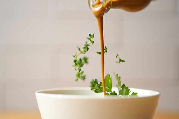 Dynamic food styling shot capturing sauce being drizzled over dish with herbs scattered for movement