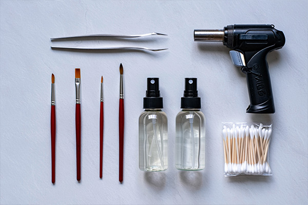 Food styling tools arranged in flat lay including tweezers, brushes, spray bottles, and kitchen torch