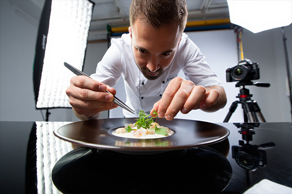 Professional food stylist using tweezers to arrange garnish on plate during photography session