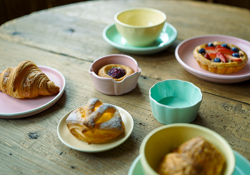 A photo of a rustic wooden table set with pastel-colored ceramic dishes and freshly baked pastries