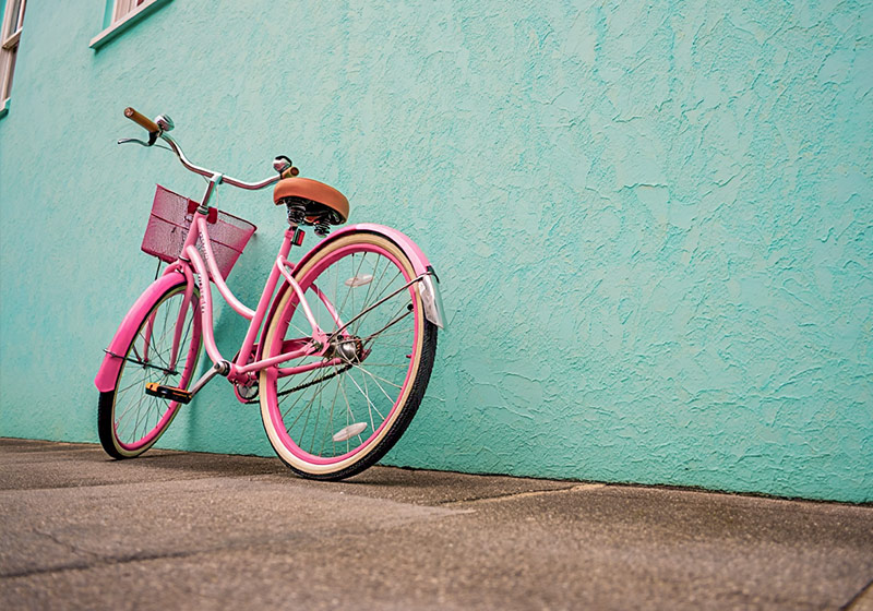 A photo of a pastel-colored vintage bicycle leaning against a soft mint-green wall on a quiet street