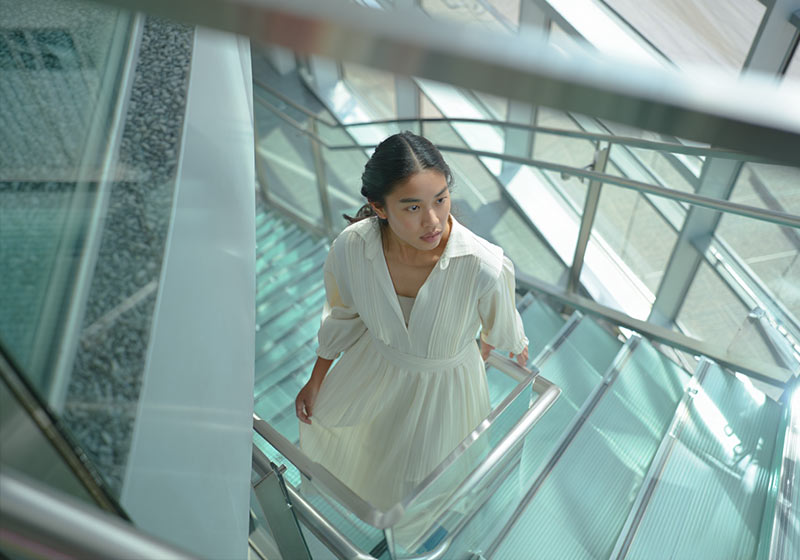 Before - a woman in a flowing dress standing on a modern glass staircase inside an office building
