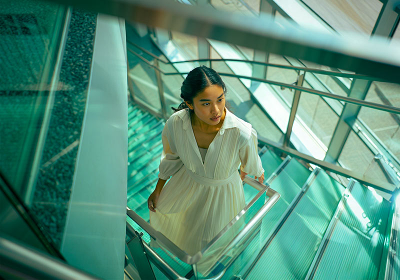 After - a woman in a flowing dress standing on a modern glass staircase inside an office building