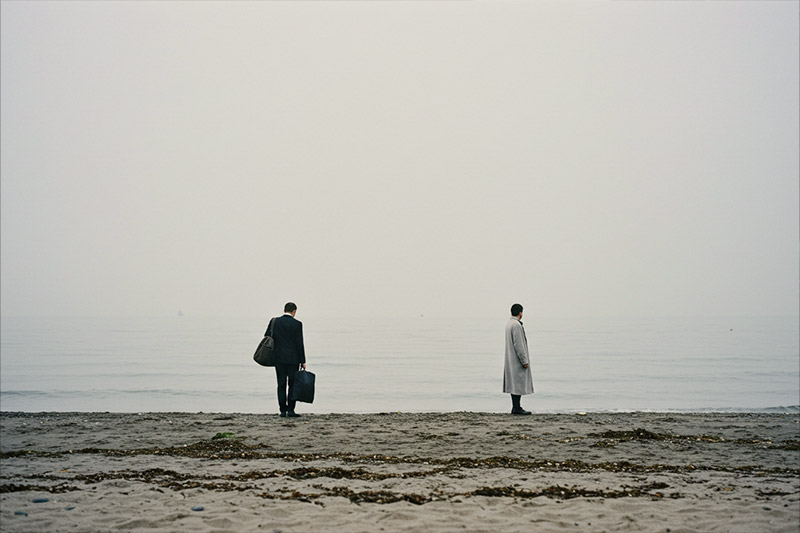 minimalist beach scene with two figures standing far apart, facing away from each