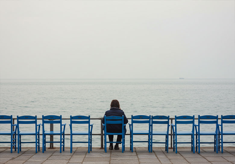 before - one lone woman sitting on a chair by the sea
