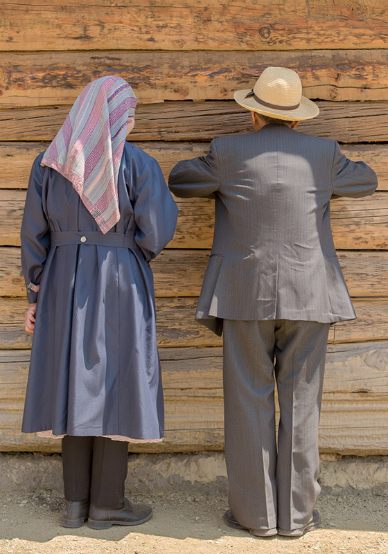 Two people stand with their backs to the camera against a weathered wooden wall