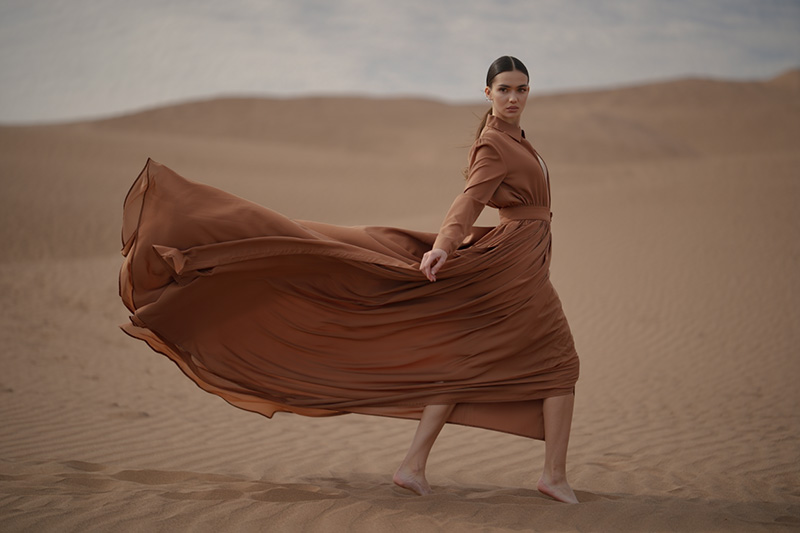before - model posing in a flowing earthy-brown dress against a desert backdrop