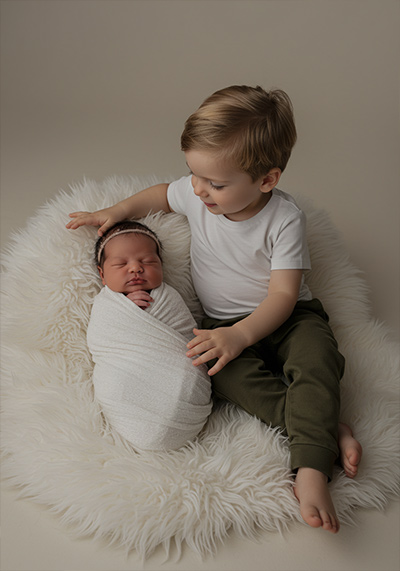 before - a newborn swaddled in a white blanket older child sitting beside