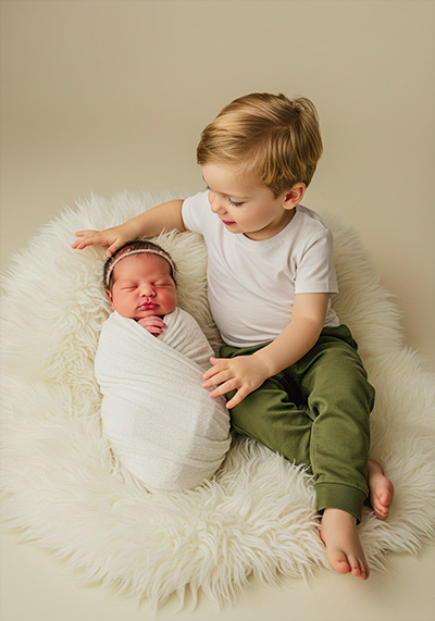 preset example - a newborn swaddled in a white blanket older child sitting beside