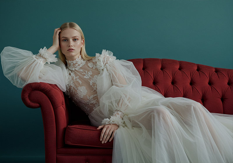 before - fashion photo of a poised model with sleek, straight blonde hair on a deep red tufted velvet sofa